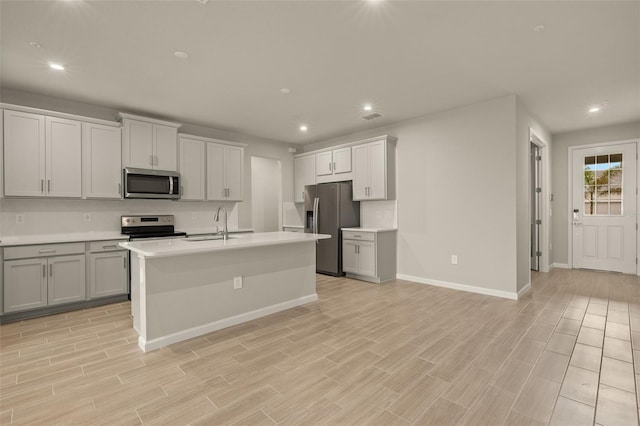 kitchen featuring gray cabinetry, sink, a center island with sink, and appliances with stainless steel finishes