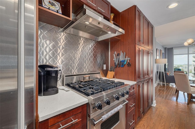 kitchen featuring exhaust hood, light hardwood / wood-style flooring, tasteful backsplash, light stone counters, and stainless steel appliances