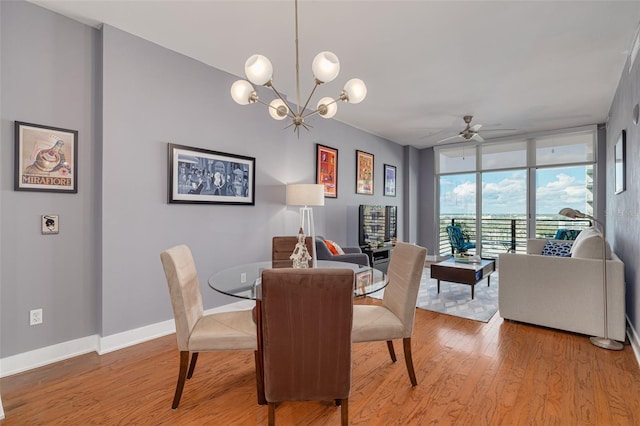 dining space with light wood-type flooring, ceiling fan with notable chandelier, and a wall of windows