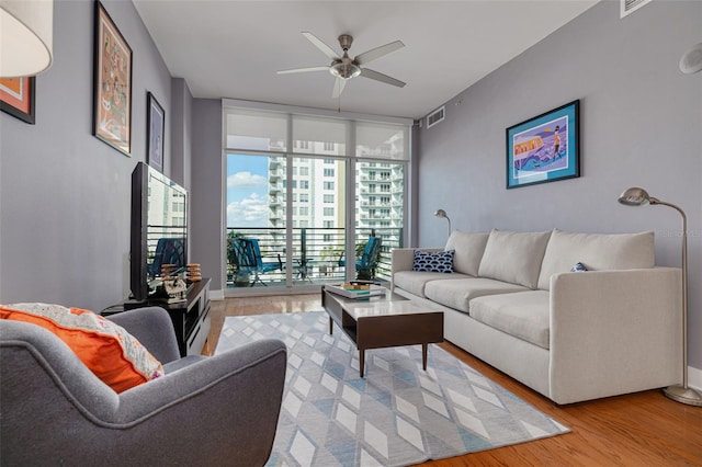 living room featuring ceiling fan, light hardwood / wood-style floors, and a wall of windows