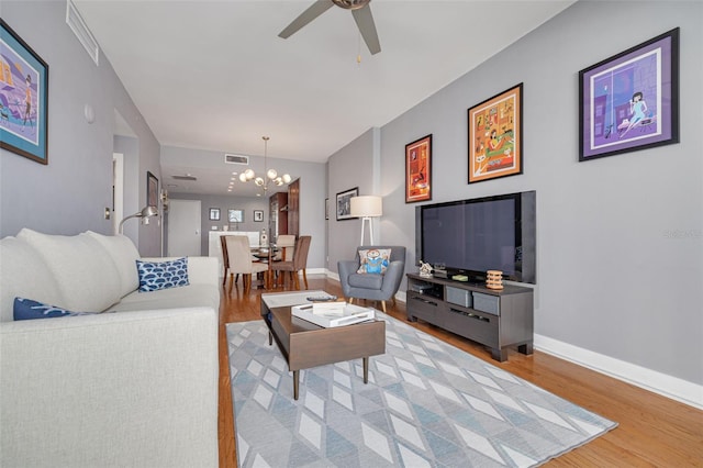 living room featuring ceiling fan with notable chandelier and light wood-type flooring