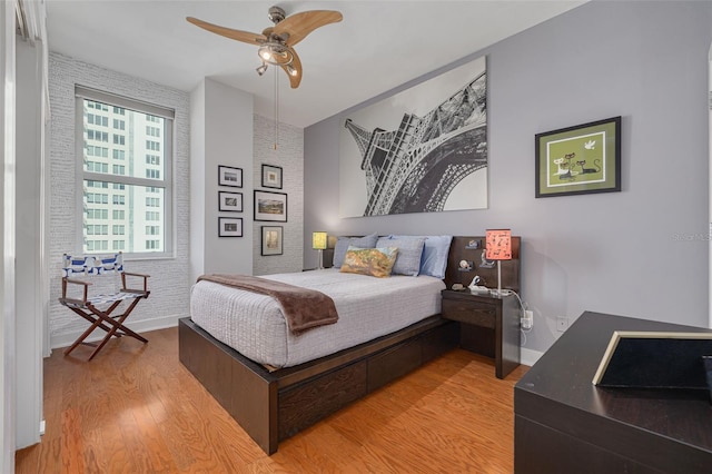 bedroom featuring ceiling fan, brick wall, and light wood-type flooring