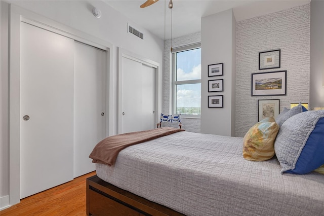 bedroom featuring hardwood / wood-style floors, ceiling fan, and multiple closets