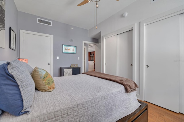 bedroom featuring light wood-type flooring, two closets, and ceiling fan