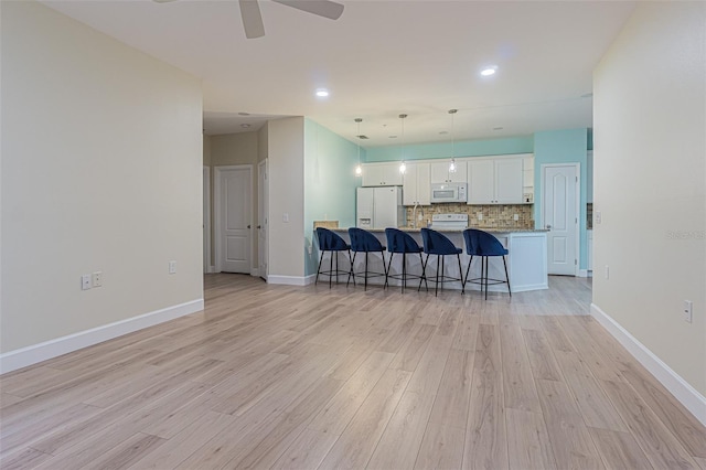 kitchen featuring decorative backsplash, kitchen peninsula, white appliances, pendant lighting, and white cabinets