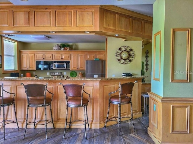 kitchen featuring stainless steel appliances, light stone counters, and a breakfast bar area