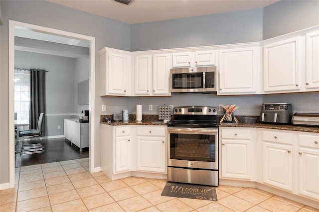 kitchen with white cabinets, appliances with stainless steel finishes, light tile patterned floors, and dark stone countertops