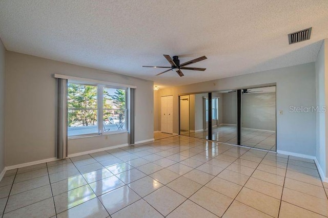 unfurnished bedroom with a textured ceiling, ceiling fan, multiple closets, and light tile patterned flooring