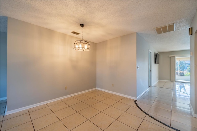 tiled empty room featuring a notable chandelier and a textured ceiling