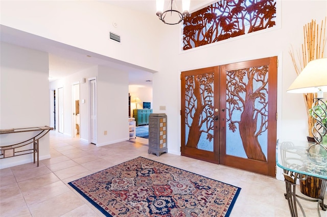 foyer entrance featuring french doors, a towering ceiling, a chandelier, and light tile patterned floors