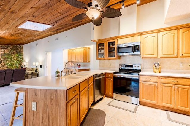 kitchen with kitchen peninsula, appliances with stainless steel finishes, a skylight, sink, and light tile patterned flooring