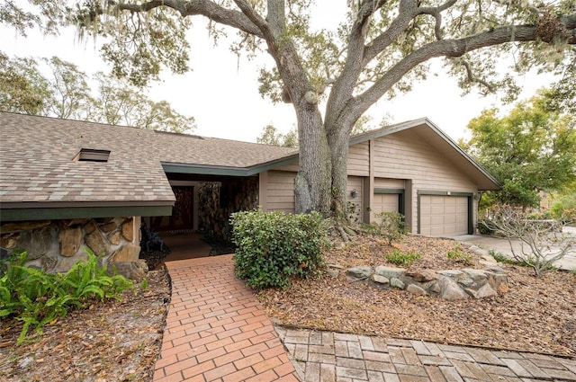 view of front facade featuring a garage, stone siding, concrete driveway, and roof with shingles