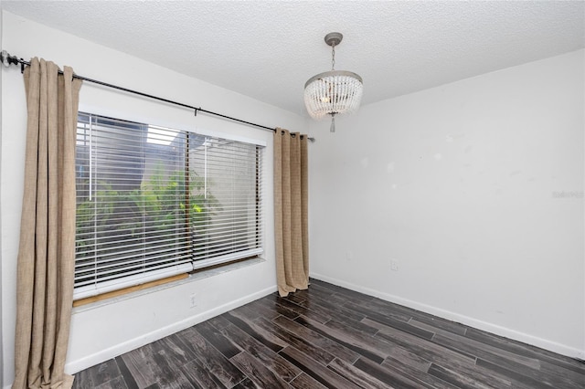 empty room with a notable chandelier, dark hardwood / wood-style flooring, and a textured ceiling