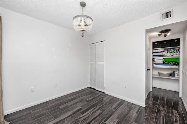 unfurnished bedroom featuring a textured ceiling, a closet, dark hardwood / wood-style flooring, and a chandelier