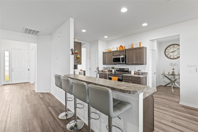 kitchen with a kitchen bar, kitchen peninsula, light wood-type flooring, and appliances with stainless steel finishes