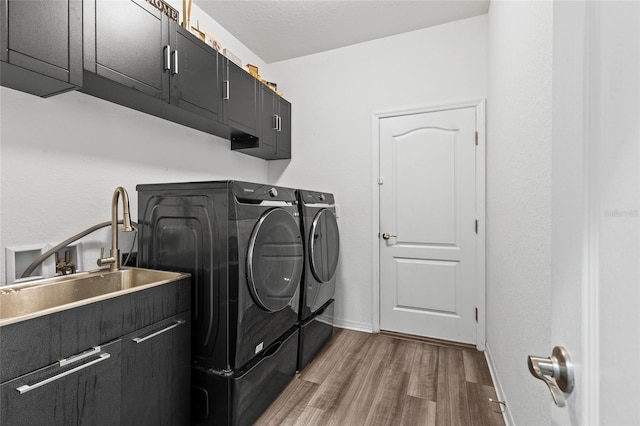 clothes washing area featuring washing machine and dryer, sink, cabinets, and wood-type flooring