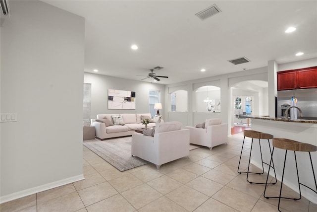 tiled living room with ceiling fan with notable chandelier and sink