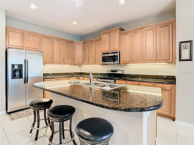 kitchen featuring light brown cabinets, dark stone counters, light tile patterned floors, an island with sink, and stainless steel appliances