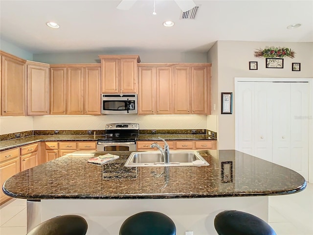 kitchen featuring sink, stainless steel appliances, dark stone countertops, a kitchen bar, and a center island with sink