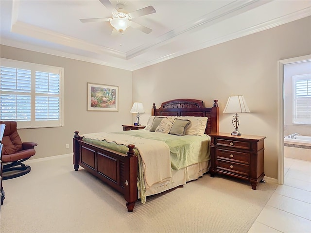 carpeted bedroom featuring a tray ceiling, ensuite bath, ceiling fan, and multiple windows