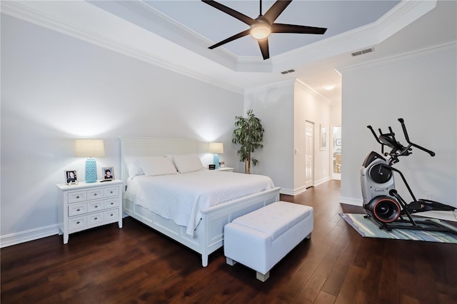 bedroom with ensuite bath, ceiling fan, dark wood-type flooring, a tray ceiling, and ornamental molding