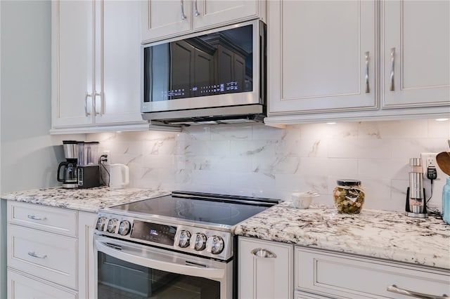 kitchen featuring tasteful backsplash, white cabinetry, light stone countertops, and stainless steel appliances