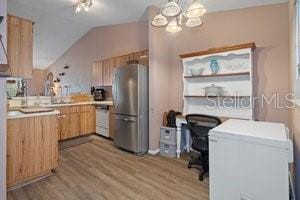 kitchen with stainless steel refrigerator, white dishwasher, vaulted ceiling, light brown cabinetry, and light wood-type flooring