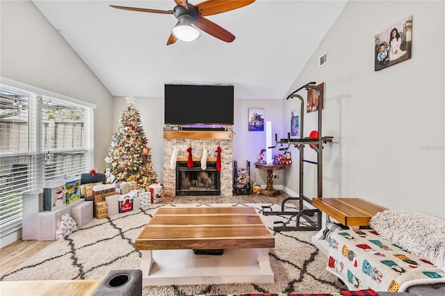 living room with light hardwood / wood-style floors, vaulted ceiling, ceiling fan, and a stone fireplace