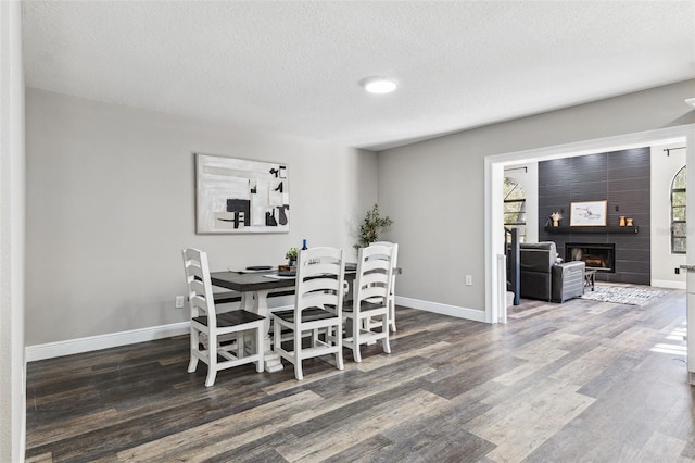 dining space featuring a textured ceiling, a large fireplace, and dark wood-type flooring