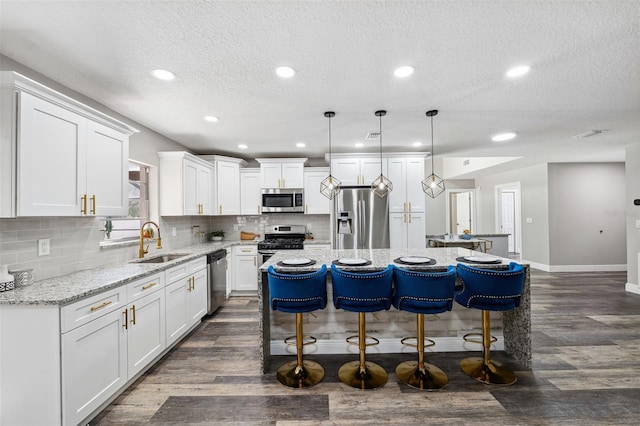 kitchen featuring appliances with stainless steel finishes, sink, decorative light fixtures, white cabinets, and a kitchen island