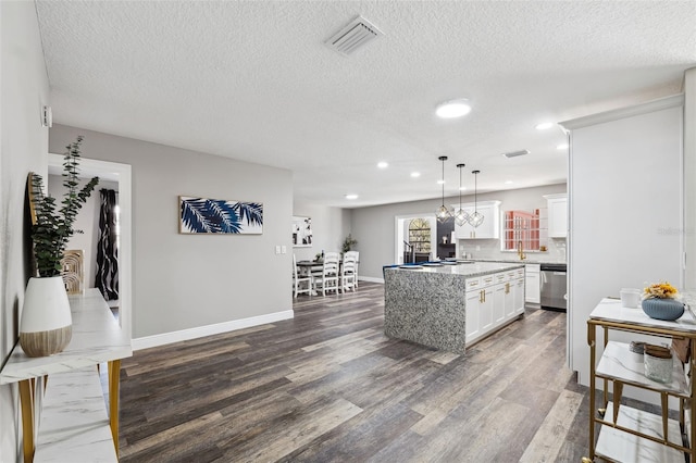 kitchen with pendant lighting, a center island, white cabinets, stainless steel dishwasher, and light stone counters