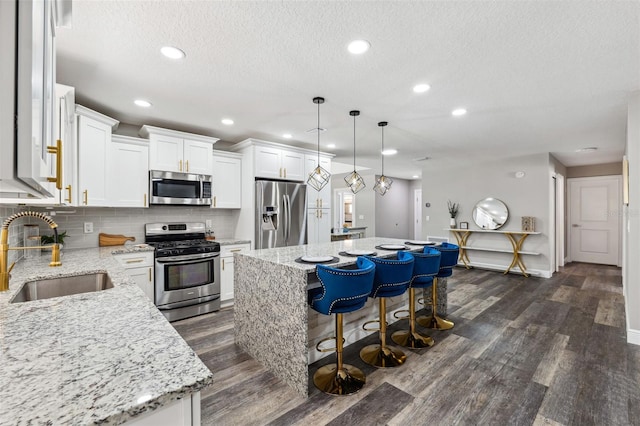 kitchen with a center island, sink, light stone counters, white cabinetry, and stainless steel appliances