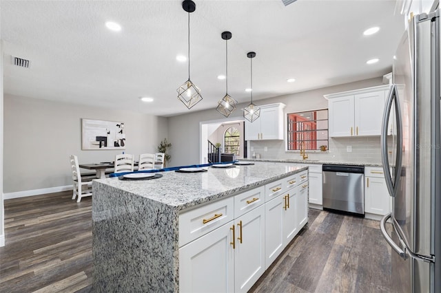 kitchen featuring appliances with stainless steel finishes, dark wood-type flooring, decorative light fixtures, white cabinets, and a center island