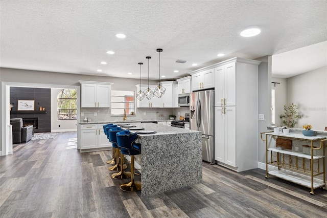 kitchen featuring appliances with stainless steel finishes, dark wood-type flooring, white cabinets, a center island, and hanging light fixtures