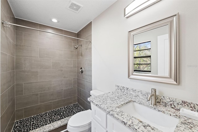 bathroom with a tile shower, vanity, a textured ceiling, and toilet