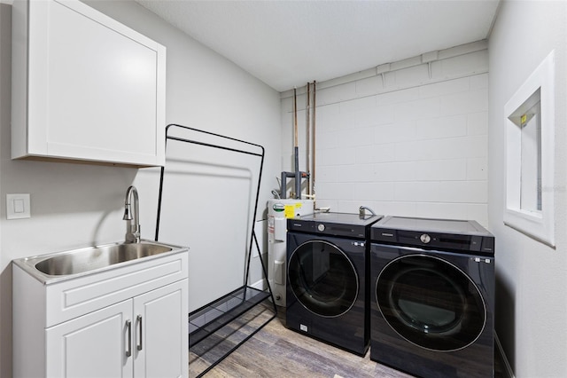 laundry room featuring cabinets, water heater, sink, light hardwood / wood-style flooring, and washing machine and dryer