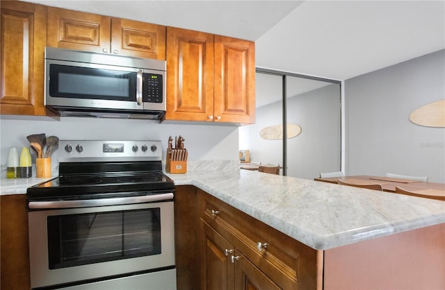 kitchen with light stone countertops, appliances with stainless steel finishes, and kitchen peninsula