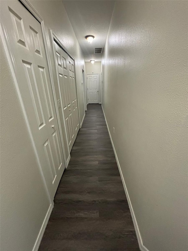 hall with a textured ceiling and dark wood-type flooring