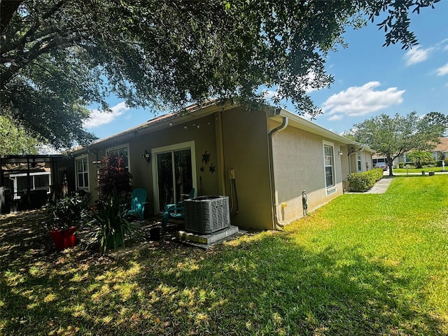 rear view of house with central air condition unit and a lawn