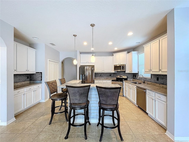 kitchen featuring decorative light fixtures, white cabinets, stainless steel appliances, and a kitchen island