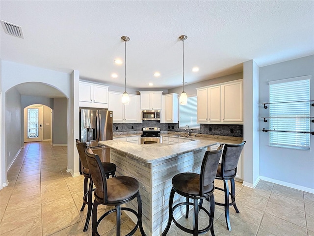 kitchen with decorative light fixtures, a center island, decorative backsplash, appliances with stainless steel finishes, and light tile patterned floors