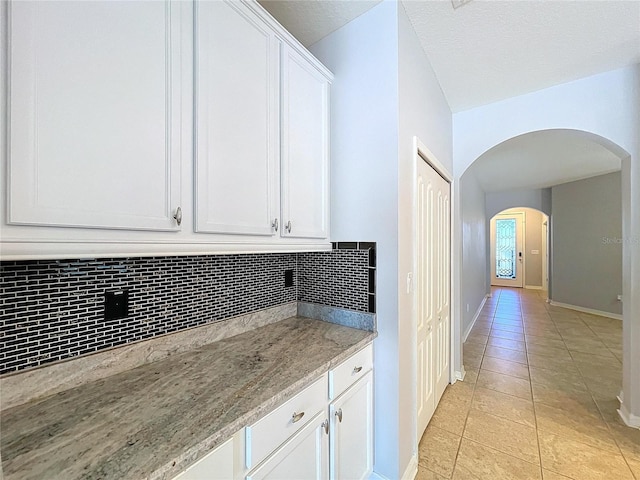 kitchen featuring light stone countertops, backsplash, white cabinetry, and light tile patterned floors