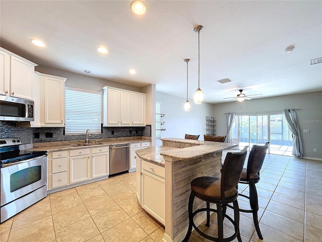 kitchen featuring a kitchen island, sink, hanging light fixtures, appliances with stainless steel finishes, and light stone counters