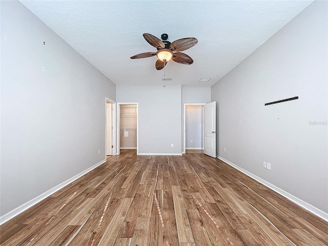 unfurnished bedroom featuring a spacious closet, hardwood / wood-style floors, a textured ceiling, a closet, and ceiling fan