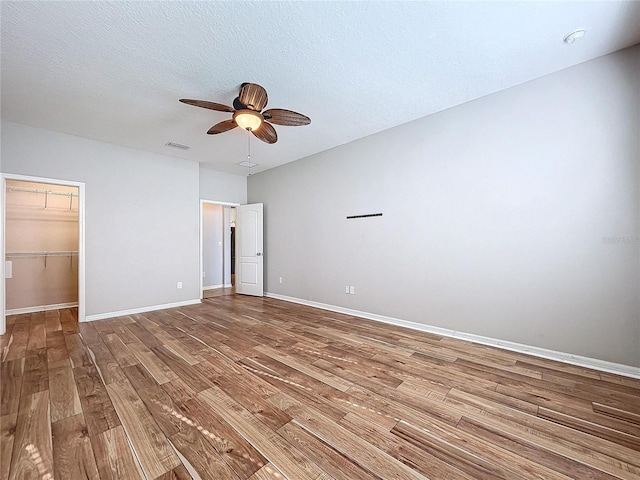 unfurnished bedroom with ceiling fan, hardwood / wood-style floors, a spacious closet, a textured ceiling, and a closet