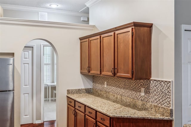 kitchen with light stone counters, backsplash, stainless steel fridge, and ornamental molding