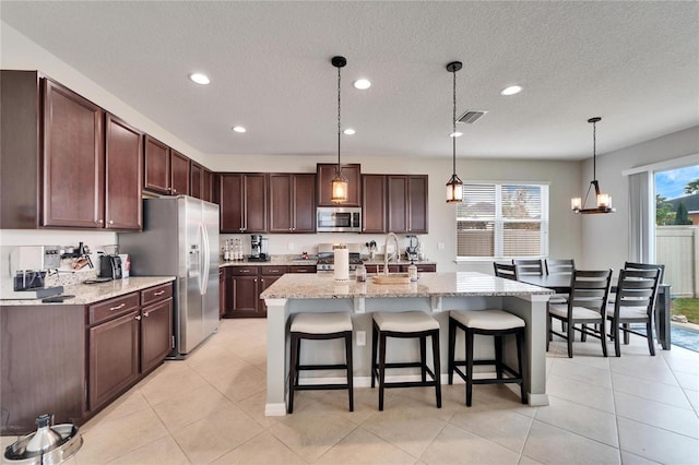 kitchen with appliances with stainless steel finishes, a wealth of natural light, a breakfast bar, a kitchen island with sink, and pendant lighting