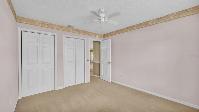 unfurnished bedroom with ceiling fan, light colored carpet, a textured ceiling, and two closets