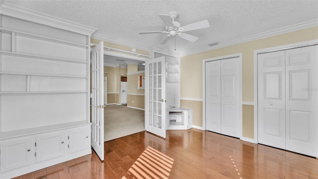 unfurnished bedroom featuring multiple closets, ceiling fan, french doors, and crown molding