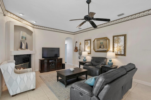 tiled living room featuring a premium fireplace, ceiling fan, and crown molding